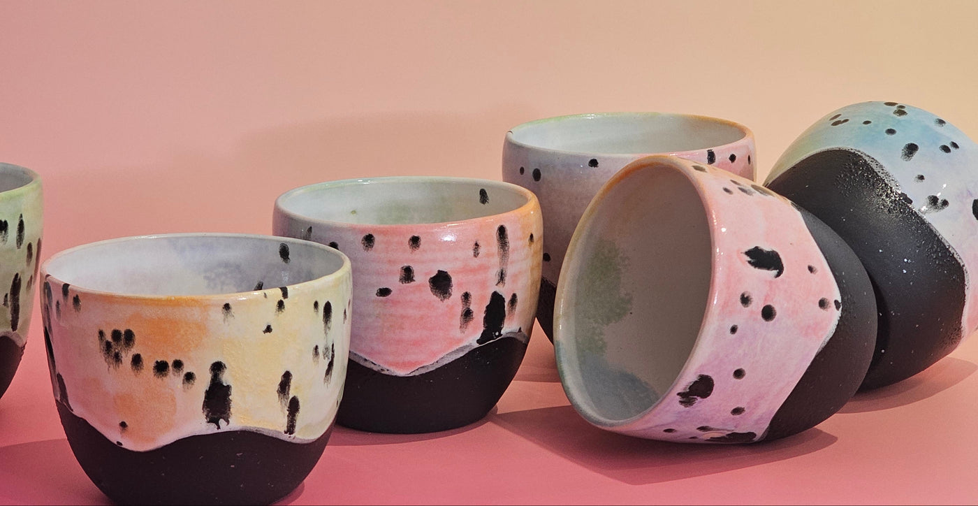 Set of ceramic cups with black and white speckled pattern on a pink background